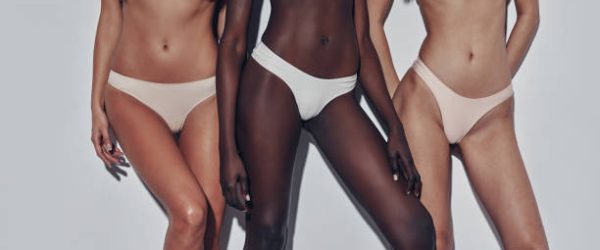 Close up of three attractive mixed race women in lingerie standing against grey background